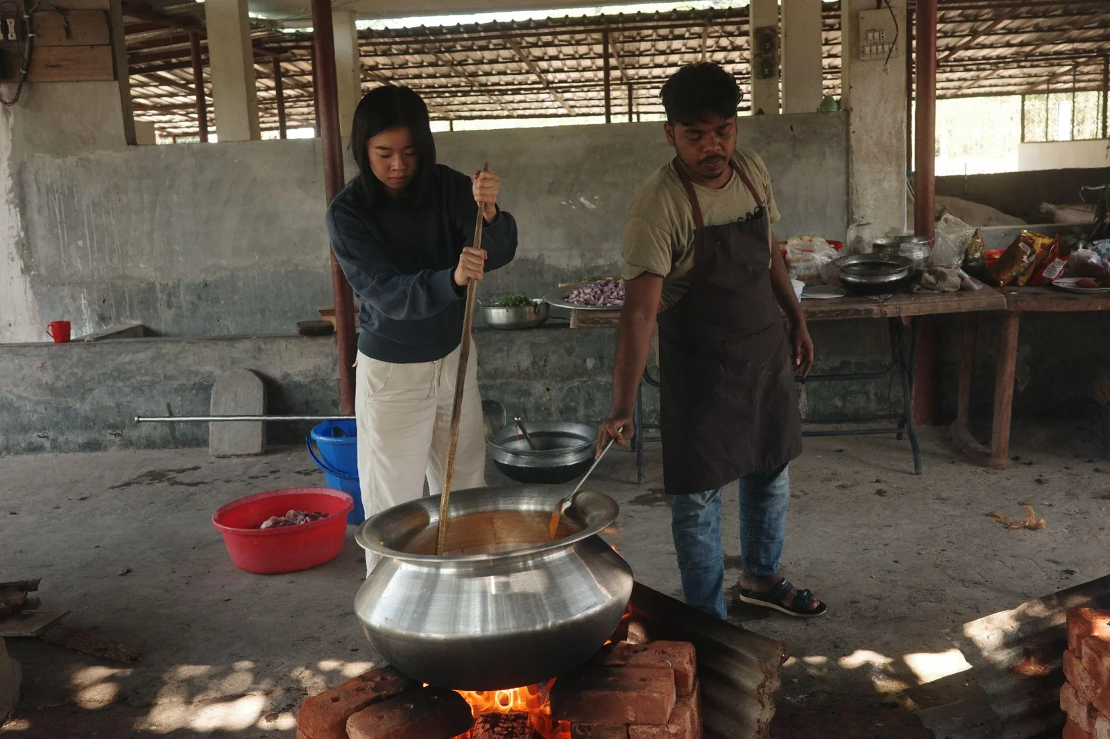 Two cooks working over a wide pan on an open fire