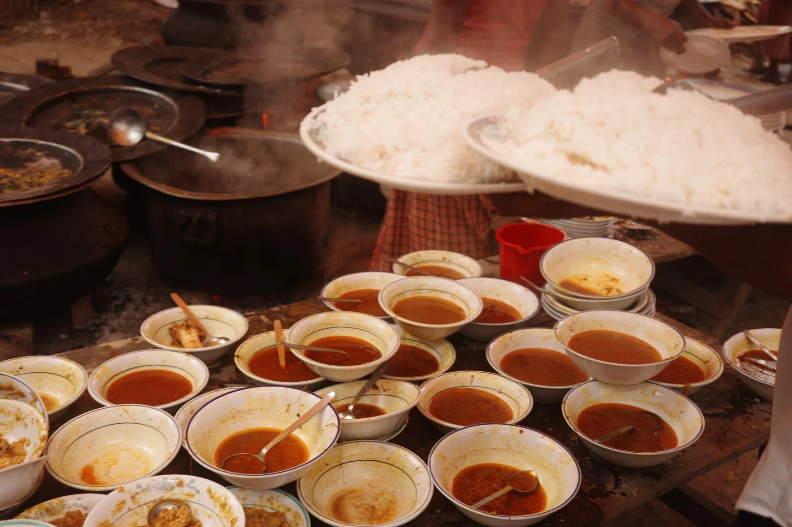 Dozens of bowls of curry laid out beside steaming platters of rice