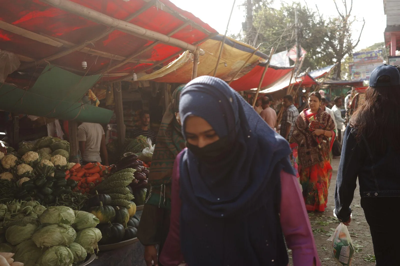 A woman passing stalls piled with cabbages and greens