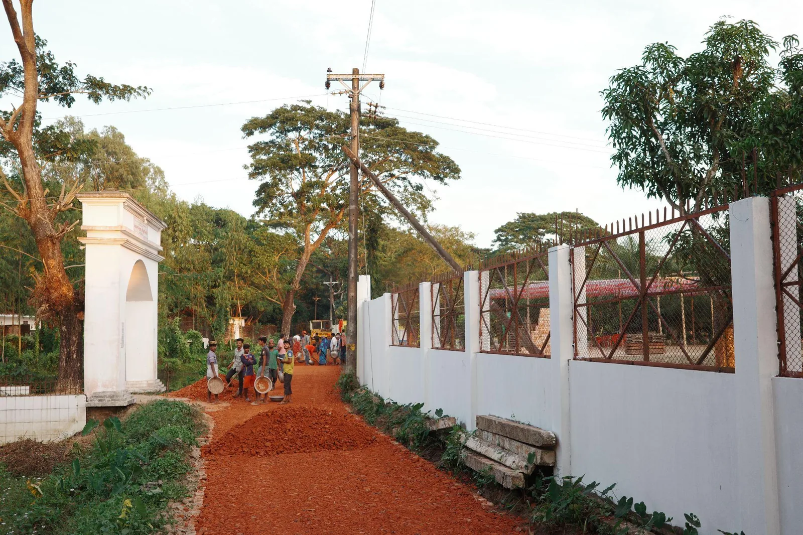 A red dirt road running between white walls out towards the village